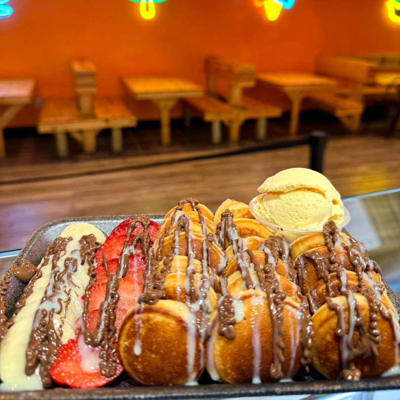 Mini pancakes with chocolate and white drizzle, sliced strawberries, bananas, and a scoop of ice cream.