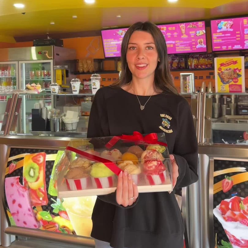 A woman in a Que Pasa Michoacana shirt holds a clear box of colorful ice cream scoops.